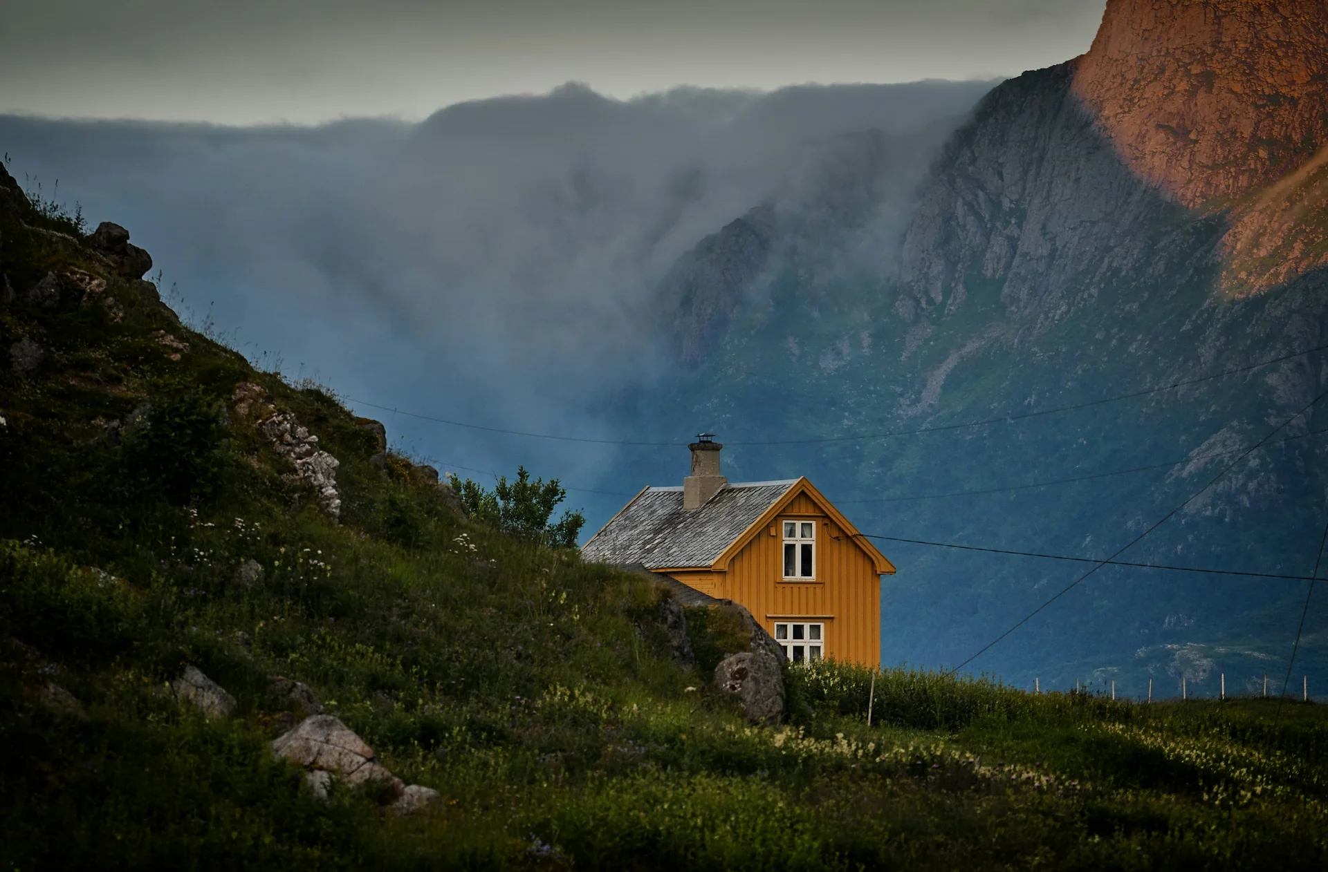 Casa amarilla aislada entre montañas y niebla en una zona rural.